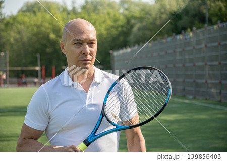 Mature man playing tennis outdoors on sunny sports court 139856403