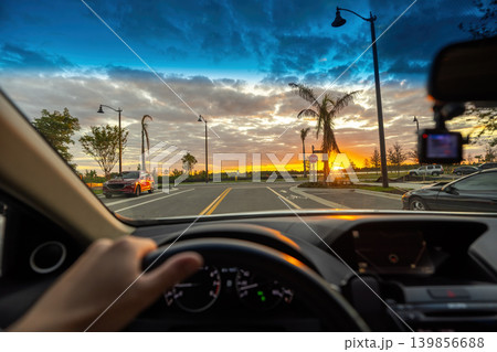 Point of view driving along palm-lined street at sunset with steady traffic flow, capturing travel, relaxation and urban mobility. 139856688