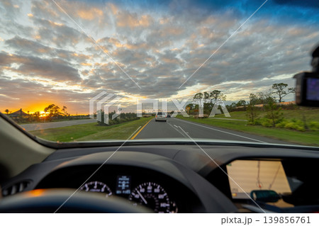 POV commute through rural town district, dashboard visible, cars merging at intersection, street lights turning on as evening approaches. 139856761