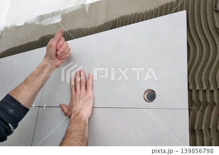 Worker hands putting ceramic tiles on the wall. Worker hands putting ceramic tiles on the wall. 139856798