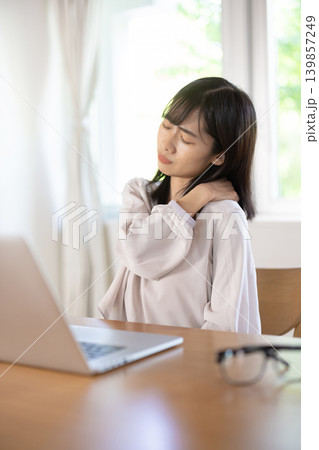 パソコン作業中に肩に手を当てて眉をしかめる日本人の若い女性 139857249