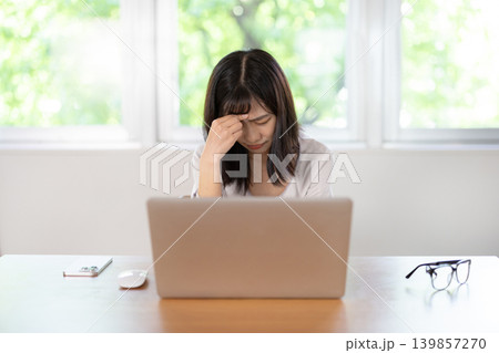 パソコン作業中に頭に手を当てて眉をしかめる日本人の若い女性 パソコン作業中に頭に手を当てて眉をしかめる日本人の若い女性 139857270