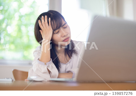 パソコン作業中に頭に手を当てて眉をしかめる日本人の若い女性 139857276