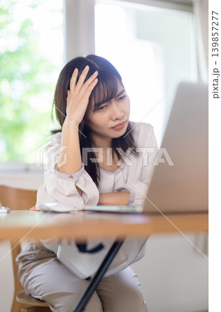 パソコン作業中に頭に手を当てて眉をしかめる日本人の若い女性 139857277