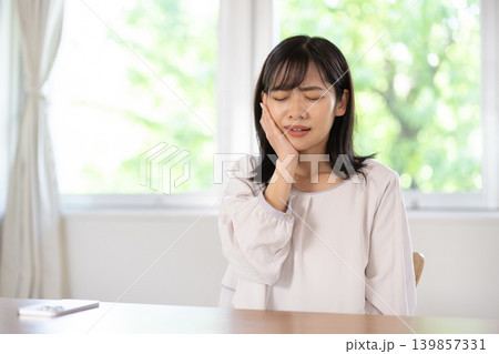 頬を押さえて痛そうな表情をする日本人の若い女性 139857331