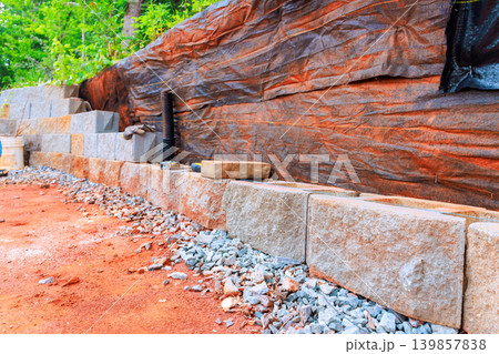 Construction workers lay stones to create retaining wall in yard with gravel dirt. Construction workers lay stones to create retaining wall in yard with gravel dirt. 139857838