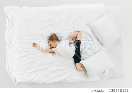Little girl sleeping diagonally across white bed in airy minimalist bedroom. Little girl sleeping diagonally across white bed in airy minimalist bedroom. 139858121