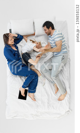 Laughing family playing on white bed with tablet nearby in bright bedroom. Laughing family playing on white bed with tablet nearby in bright bedroom. 139858132