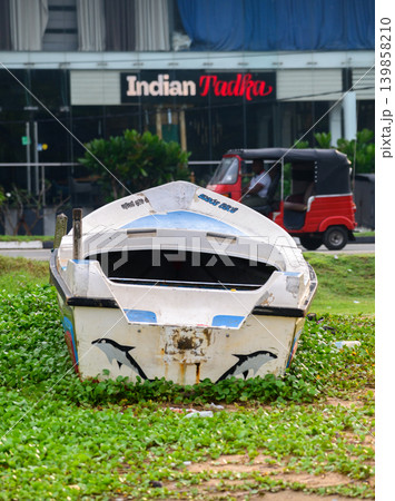 Abandoned fishing boat on urban coastal roadside with storefront background. Abandoned fishing boat on urban coastal roadside with storefront background. 139858210