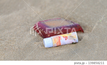 Plastic cosmetic tube discarded on a sandy beach. Coastal pollution, marine litter, and environmental contamination concept 139858211
