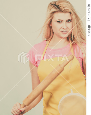 Woman wearing apron holding colander and rolling pin Woman wearing apron holding colander and rolling pin 139858916