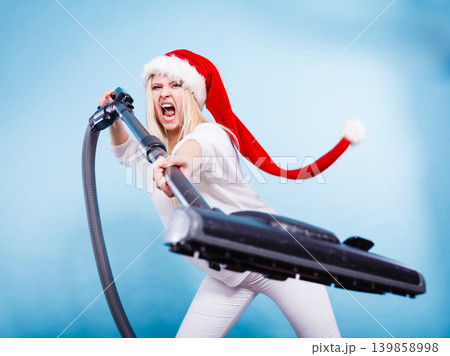 Angry girl in santa helper hat with vacuum cleaner Angry girl in santa helper hat with vacuum cleaner 139858998