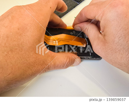 A technician repairs a modern smartphone with exposed internal components, battery, and tools on a white workbench. Concept for electronics repair and mobile device servicing A technician repairs a modern smartphone with exposed internal components, battery, and tools on a white workbench. Concept for electronics repair and mobile device servicing 139859037