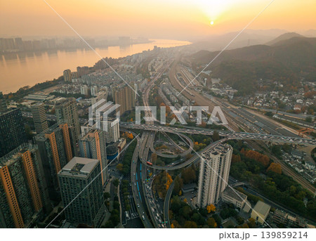 High angle aerial view of an urban landscape bathed in warm sunset glow, featuring a large river, high-rise residential towers, a busy multi-level freeway, and distant mountains High angle aerial view of an urban landscape bathed in warm sunset glow, featuring a large river, high-rise residential towers, a busy multi-level freeway, and distant mountains 139859214