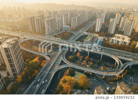 Cars move on a multi-level highway interchange cutting through a city filled with numerous tall residential and commercial structures 139859232