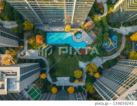 Overhead view of a large urban residential complex. Modern high-rise buildings surround a park with bright blue swimming pool and little playground 139859243