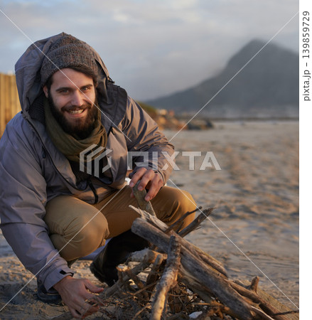 Portrait, smile and man at beach with campfire on holiday, vacation or travel toe prepare for winter outdoor alone. Happy person, wood and adventure at seashore, leisure and recreation in Canada 139859729