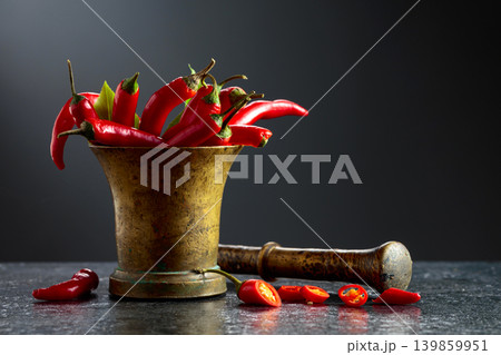 Fresh red chili peppers in old brass mortar on a black table. Fresh red chili peppers in old brass mortar on a black table. 139859951
