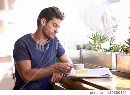 Man, coffee shop and relaxing with newspaper and cup, hot beverage and article for information. Male person, restaurant and reading paper for announcement, print and story for update and tea at cafe 139860133