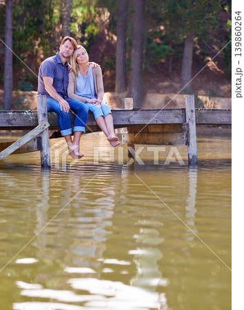 Mature couple, together and relax in lake, countryside and commitment with love in marriage. Happiness, smile and hug by partner, family and woman with man sitting on dock for sightseeing in nature Mature couple, together and relax in lake, countryside and commitment with love in marriage. Happiness, smile and hug by partner, family and woman with man sitting on dock for sightseeing in nature 139860264