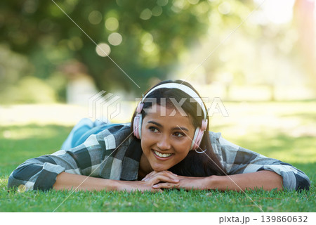 Woman, headphones and streaming music on grass, radio and internet for podcast in outdoors. Female person, happy and relaxing on lawn, weekend playlist and subscription for audio or sound on vacation Woman, headphones and streaming music on grass, radio and internet for podcast in outdoors. Female person, happy and relaxing on lawn, weekend playlist and subscription for audio or sound on vacation 139860632