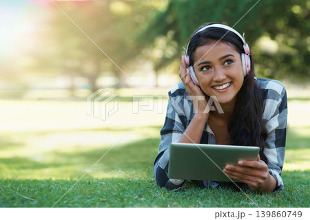 Woman, headphones and streaming podcast on tablet, learning and internet for education on grass in outdoors. Female person, happy and relaxing on lawn, knowledge and student subscription for info Woman, headphones and streaming podcast on tablet, learning and internet for education on grass in outdoors. Female person, happy and relaxing on lawn, knowledge and student subscription for info 139860749