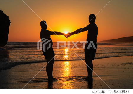Silhouette of gay couple holding hands at sunset on the beach 139860988