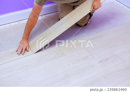 Handy worker places wooden floor board in room with purple walls while working on home improvement task. 139861460