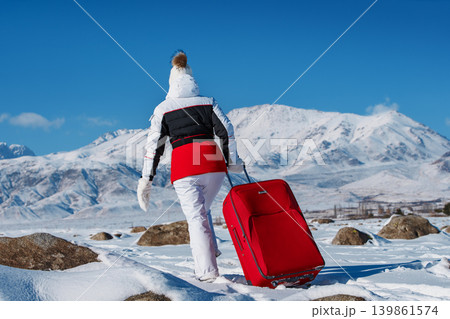 Young woman traveling with red suitcase on winter mountains background Young woman traveling with red suitcase on winter mountains background 139861574
