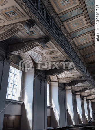 Natural light streams through tall, paned windows, casting sharp highlights across the multi-tiered neoclassical space. An elegant stone balcony stretches along the upper wall, supported by heavy, Natural light streams through tall, paned windows, casting sharp highlights across the multi-tiered neoclassical space. An elegant stone balcony stretches along the upper wall, supported by heavy, 139861718
