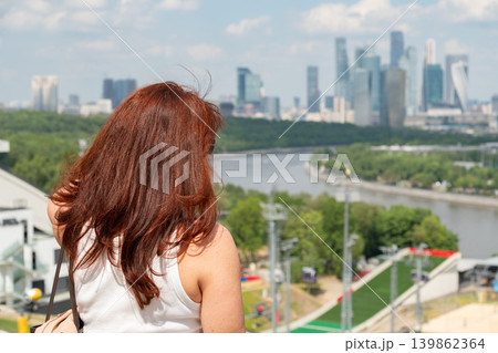 Red-haired woman overlooks Moscow River and Moscow City skyline from observation deck with modern skyscrapers, green riverside landscape. Tourism, urban lifestyle, city travel, panoramic destination Red-haired woman overlooks Moscow River and Moscow City skyline from observation deck with modern skyscrapers, green riverside landscape. Tourism, urban lifestyle, city travel, panoramic destination 139862364