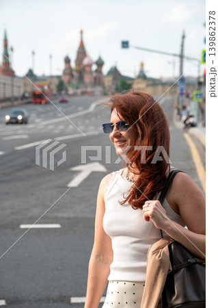 Woman in sunglasses walks on Moscow street with Saint Basil Cathedral, wide roadway and city traffic in background. Tourism, city travel advertising, personal branding, social media 139862378