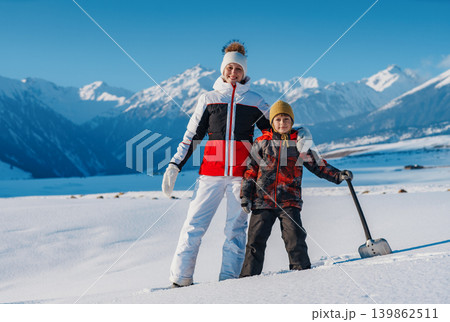 Woman and child with shovel standing on winter mountains background Woman and child with shovel standing on winter mountains background 139862511