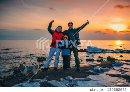 Father, mother, son and dog happy family posing on lake sunset background at winter season Father, mother, son and dog happy family posing on lake sunset background at winter season 139862685