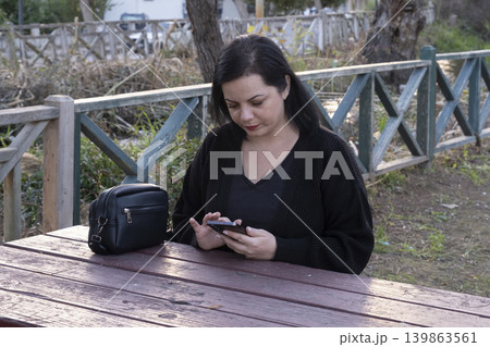 Woman Using Smartphone While Sitting on Park Bench. Woman Using Smartphone While Sitting on Park Bench. 139863561