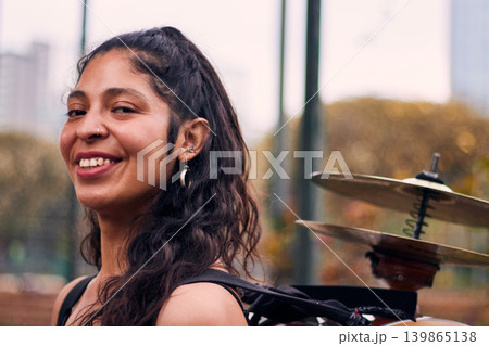 Beautiful dark-haired Latina woman posing with a drum and cymbals on her back, full of joy, a chinchinera, a street musician who dances and plays her drum in the streets. Chilean heritage Beautiful dark-haired Latina woman posing with a drum and cymbals on her back, full of joy, a chinchinera, a street musician who dances and plays her drum in the streets. Chilean heritage 139865138
