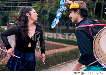 Adult couple of urban dancers, happily playing and dancing the cueca with a bass drum on their backs outdoors, Chilean chinchineros, street musicians who play the bass drum and dance in the streets Adult couple of urban dancers, happily playing and dancing the cueca with a bass drum on their backs outdoors, Chilean chinchineros, street musicians who play the bass drum and dance in the streets 139865147
