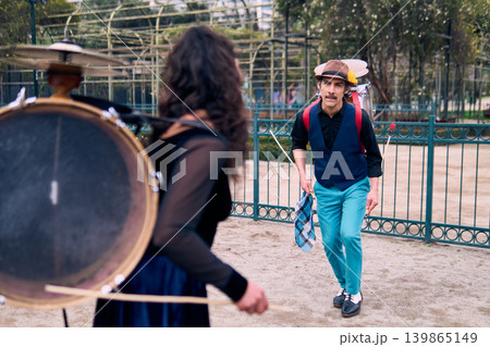 Adult couple of urban dancers, happily playing and dancing the cueca with a bass drum on their backs outdoors, Chilean chinchineros, street musicians who play the bass drum and dance in the streets 139865149