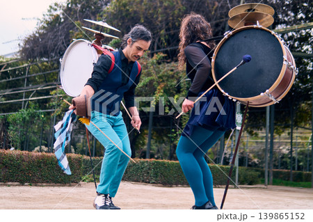 A pair of urban dancers, spinning, playing and dancing, with a bass drum on their backs outdoors, Chilean chinchineros, street musicians who play the bass drum and dance in the streets. 139865152
