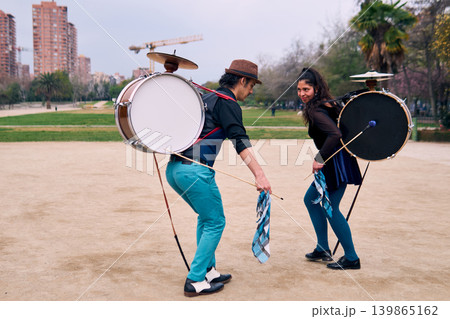 A pair of urban dancers, spinning, playing and dancing, with a bass drum on their backs outdoors, Chilean chinchineros, street musicians who play the bass drum and dance in the streets. A pair of urban dancers, spinning, playing and dancing, with a bass drum on their backs outdoors, Chilean chinchineros, street musicians who play the bass drum and dance in the streets. 139865162