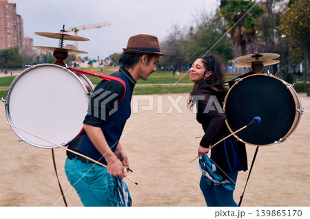 A pair of urban dancers, spinning, playing and dancing, with a bass drum on their backs outdoors, Chilean chinchineros, street musicians who play the bass drum and dance in the streets. A pair of urban dancers, spinning, playing and dancing, with a bass drum on their backs outdoors, Chilean chinchineros, street musicians who play the bass drum and dance in the streets. 139865170