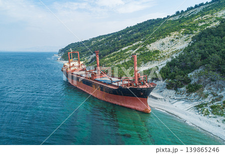 Grounded derelict cargo ship on a rocky Black Sea beach with green mountains under a bright sky Grounded derelict cargo ship on a rocky Black Sea beach with green mountains under a bright sky 139865246