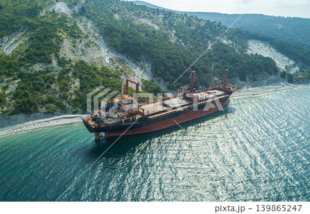 Grounded derelict cargo ship on a rocky Black Sea beach with green mountains under a bright sky Grounded derelict cargo ship on a rocky Black Sea beach with green mountains under a bright sky 139865247