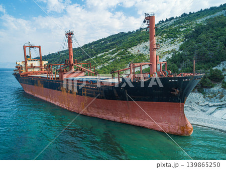 Grounded derelict cargo ship on a rocky Black Sea beach with green mountains under a bright sky Grounded derelict cargo ship on a rocky Black Sea beach with green mountains under a bright sky 139865250