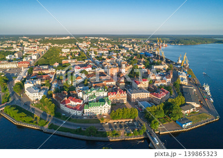 Aerial view of Vyborg's historic center, colorful buildings, busy port with cranes and ships, connecting roads by Bay of Vyborg on a bright day Aerial view of Vyborg's historic center, colorful buildings, busy port with cranes and ships, connecting roads by Bay of Vyborg on a bright day 139865323