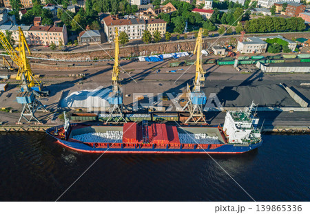 Aerial scene of an active industrial port. Yellow cranes load bulk materials into cargo ships docked at the waterfront 139865336