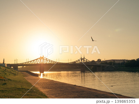 Golden sunset casts long reflections on Volga River as it flows under Starovolzhskiy Bridge in Tver, Russia Golden sunset casts long reflections on Volga River as it flows under Starovolzhskiy Bridge in Tver, Russia 139865355