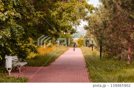 A path for walking in a city park with sunlight and shadows. Silhouette of an unrecognizable passerby, view from the back 139865902