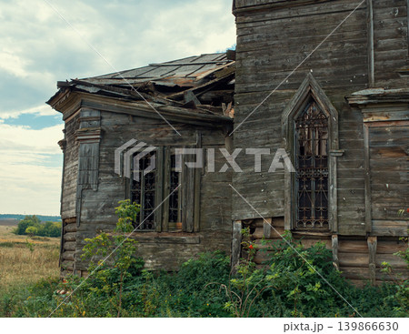 Severely decayed wooden building features a partially collapsed roof and ornate barred windows Severely decayed wooden building features a partially collapsed roof and ornate barred windows 139866630