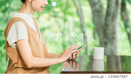 新緑の森の見えるカフェでスマホを操作する女性客の手元 新緑の森の見えるカフェでスマホを操作する女性客の手元 139867087